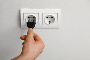 Male hand getting out plug from socket on light wall, closeup