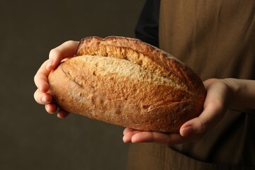 Woman with fresh loaf of bread on grey background, closeup