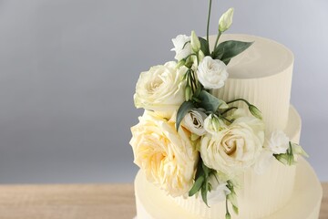 Delicious wedding cake decorated with flowers on table against grey background, closeup. Space for text