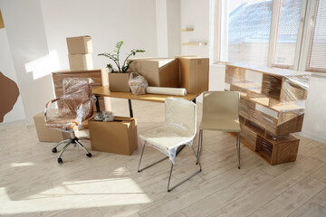 Wrapped furniture with stretch film and boxes in office on moving day