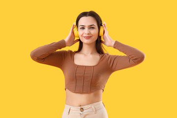 Young woman in headphones with nose piercing on yellow background