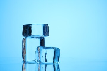 Cubes of clear ice on light blue background, closeup. Space for text