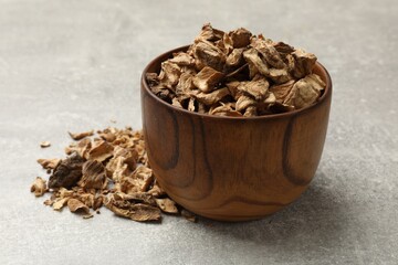 Pieces of dry chicory roots in bowl on gray textured table, closeup