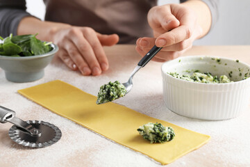 Woman making ravioli with cheese and spinach at light table, closeup