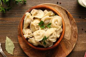Bowl with delicious boiled dumplings and parsley on wooden background