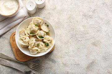 Bowl of delicious boiled dumplings with green onion and sour cream on grey background