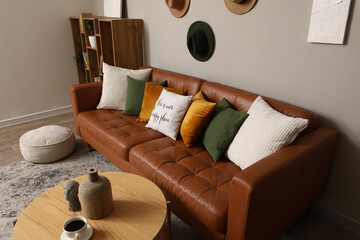 Brown leather sofa with soft pouf and wooden table near grey wall in living room