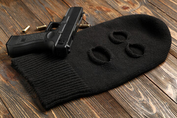 Balaclava with gun and bullets on wooden background