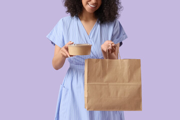 Young woman with container and paper bag on lilac background. Food delivery service