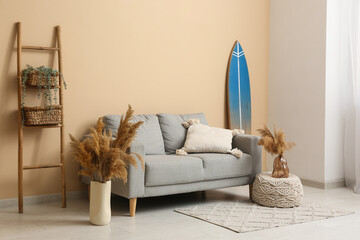 Interior of stylish living room with grey sofa, pampas grass and surfboard