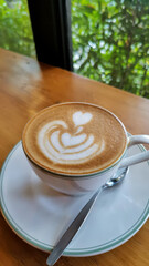 Close up of a cup of hot latte with froth art on wooden table