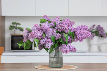 Vase with lilac flowers on table in kitchen