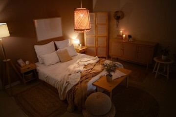 Interior of dark bedroom with folding screen, bench and glowing lamps