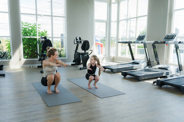 A girl stretches or exercises on a mat in a gym, with an instructor closely following her.