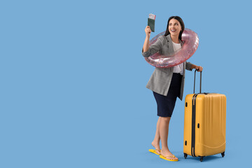 Young businesswoman with packed suitcase, swimming ring, passport and tickets on blue background....