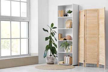 Interior of light room with bookshelf, plants and folding screen