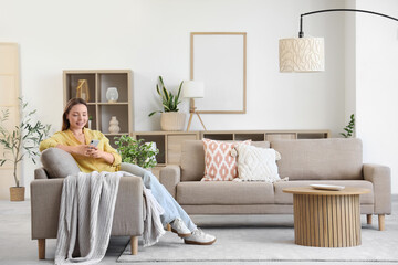 Smiling young woman using mobile phone on grey sofa in living room