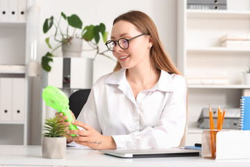 Young businesswoman with mini fan at table in office