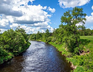 Fototapeta premium Serene River Flowing Through Lush Green Landscape Under Blue Sky