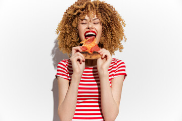 Happy young woman enjoying pizza with red sauce, wearing a striped shirt on a white background, showcasing joy and delicious food cravings