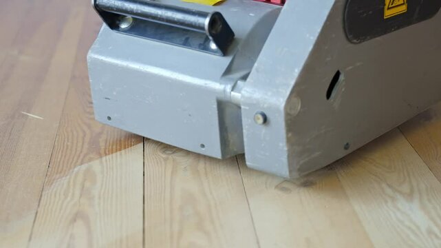 Close-up view shows a professional floor sanding machine working on a pine wood floor, revealing the sharp transition between sanded and unsanded wood, camera low, slow motion, smooth linear movement.