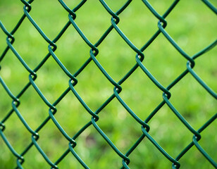 Fototapeta premium Emerald Mesh: A close-up of a verdant chain-link fence, its woven pattern creates a sense of security, set against a backdrop of a blurred green field.