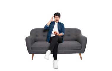Full body image of young Asian man using phone sitting on sofa on PNG background	