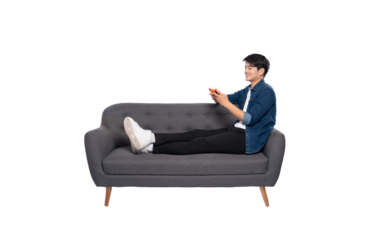 Full body image of young Asian man using phone sitting on sofa on PNG background	