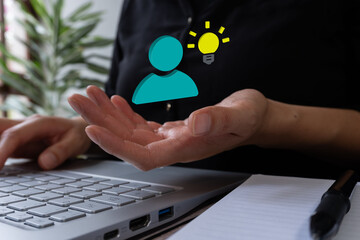 Businesswoman hand in front of computer keyboard, holding a 3D person avatar icon with light bomb