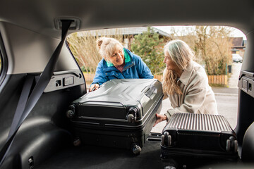 Senior caucasian lesbian couple packing their suitcase into the trunk of there car before going on a road trip vacation