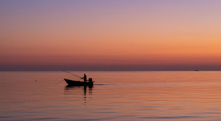 Obraz premium Solitary Fisherman in Small Boat at Sunrise Serene Ocean Scene