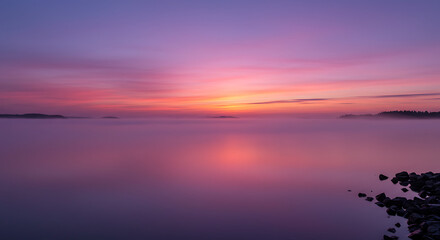 Fototapeta premium Serene Sunrise over Misty Lake Pink and Purple Sky Calm Water Rocks