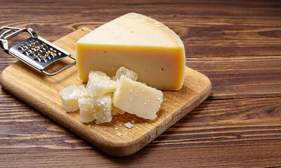 A block of cheese and grated pieces on a wooden cutting board with rustic background - Powered by Adobe