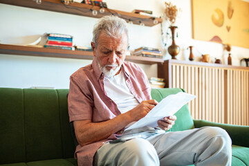 Senior man checking utility bills and using smartphone at home living room