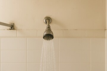 modern showerhead: A vintage-style showerhead with water flowing, mounted on a simple tiled wall, showcasing an older yet functional bathroom setup