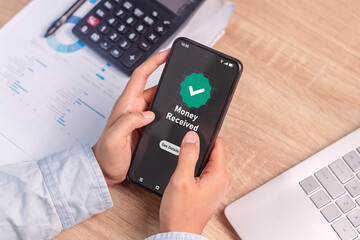 Woman's hand holding a smartphone with the phone screen showing a message of money received. Online...