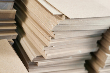 Stacks of thick paperboard ready for transformation into sustainable cardboard boxes at a manufacturing facility in the early morning light