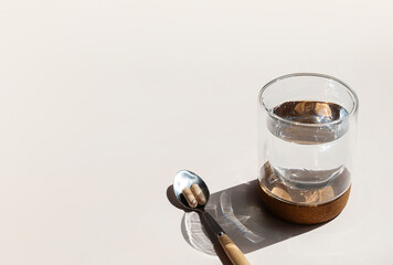 Two Pills on Spoon and Glass of Water are Ready for Daily Vitamins Intake Promoting Health and Wellness.