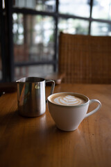 A cup of hot latte with froth art and a jar on the table