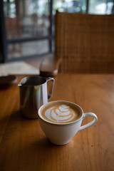 A cup of hot latte with froth art and a jar on wood table