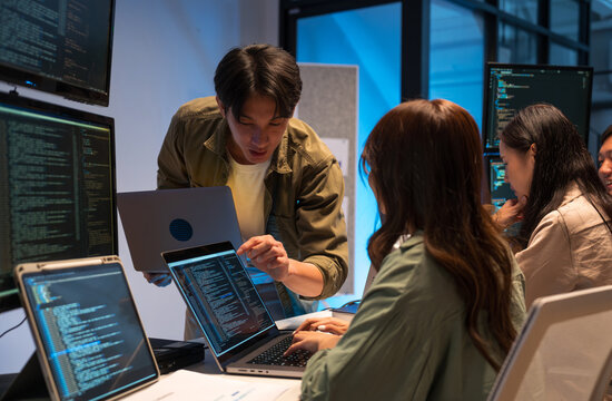 Asian man presents code during a software development meeting or coding workshop, guiding attendees through problem-solving and programming concepts in an educational setting.