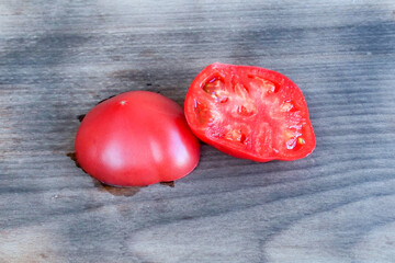  Red tomato cut in half on a gray wooden cutting board.