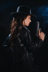 Silhouette of a female detective in a coat and hat with a gun in her hands. A book drama noir portrait in the style of detectives of the 1950s. Smoke for the atmosphere.