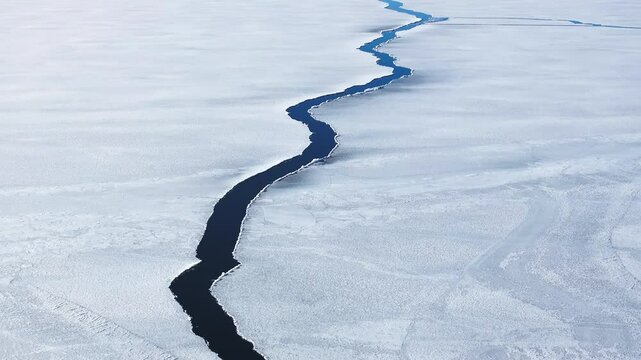 Aerial view of a crack with water in the icy frozen surface, sunny spring day