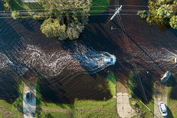 Fototapeta na wymiar Flooded Florida road with evacuating cars and surrounded with water houses in suburban residential area. Consequences of hurricane natural disaster