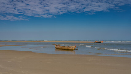 Low tide in the ocean. Wooden pirogues boats in shallow water. Reflection. Sandy beach. Blue sky, clouds. Silhouettes of fishermen in the distance. The waves are foaming. Copy space. Madagascar