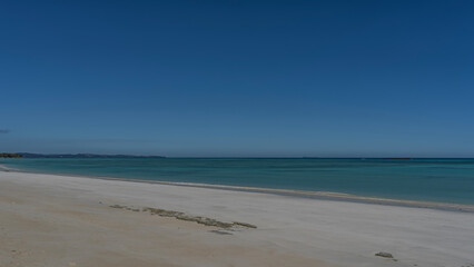 Fototapeta premium A serene minimalistic seascape without people. A calm turquoise ocean. White sandy beach. Silhouettes of mountains on the horizon. Clear blue sky. Copy space. Madagascar.