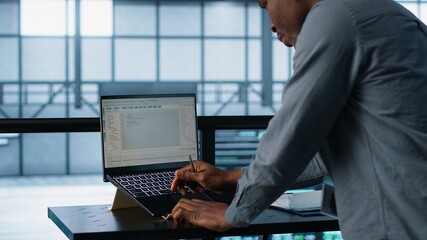 Engineer in data center coding on laptop, optimizing resource utilization, adjusting power management settings. Server room worker maintaining stable infrastructure using notebook, camera A