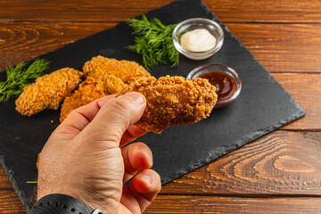 Fried chicken wing held in hand with dipping sauces on the side