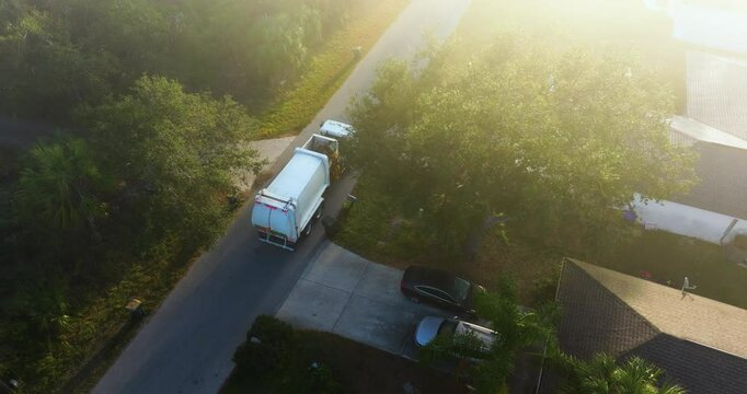 American garbage truck picking up trash bins on rural street side.